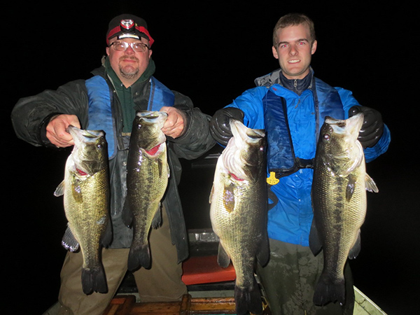 Northern fisheries supervisor Jeremy Price (left) and DNR aid Logan Halderman show off some of the big bass biologists captured during a Big Long Lake assessment of the slot limit the DNR imposed on the lake five years ago.  The largest weighed 7 pounds and all of the fish were released alive. (Indiana DNR photo)